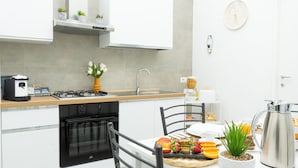 Una cocina moderna con estufa a gas, horno y pileta. Hay una mesa de comedor con fruta y una cafetera.