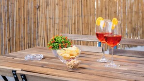 Una mesa de madera con dos vasos de bebida roja, un bol de patatas fritas y una pequeña planta.