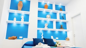 Un dormitorio con una cama, ropa de cama azul y una pared con estantes que exhiben varias esculturas.