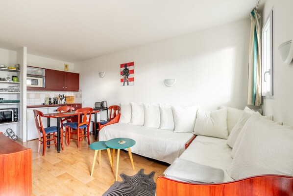Una sala de estar moderna con sofá, una mesa de comedor con sillas, una zona de cocina y una obra de arte colgada en la pared.