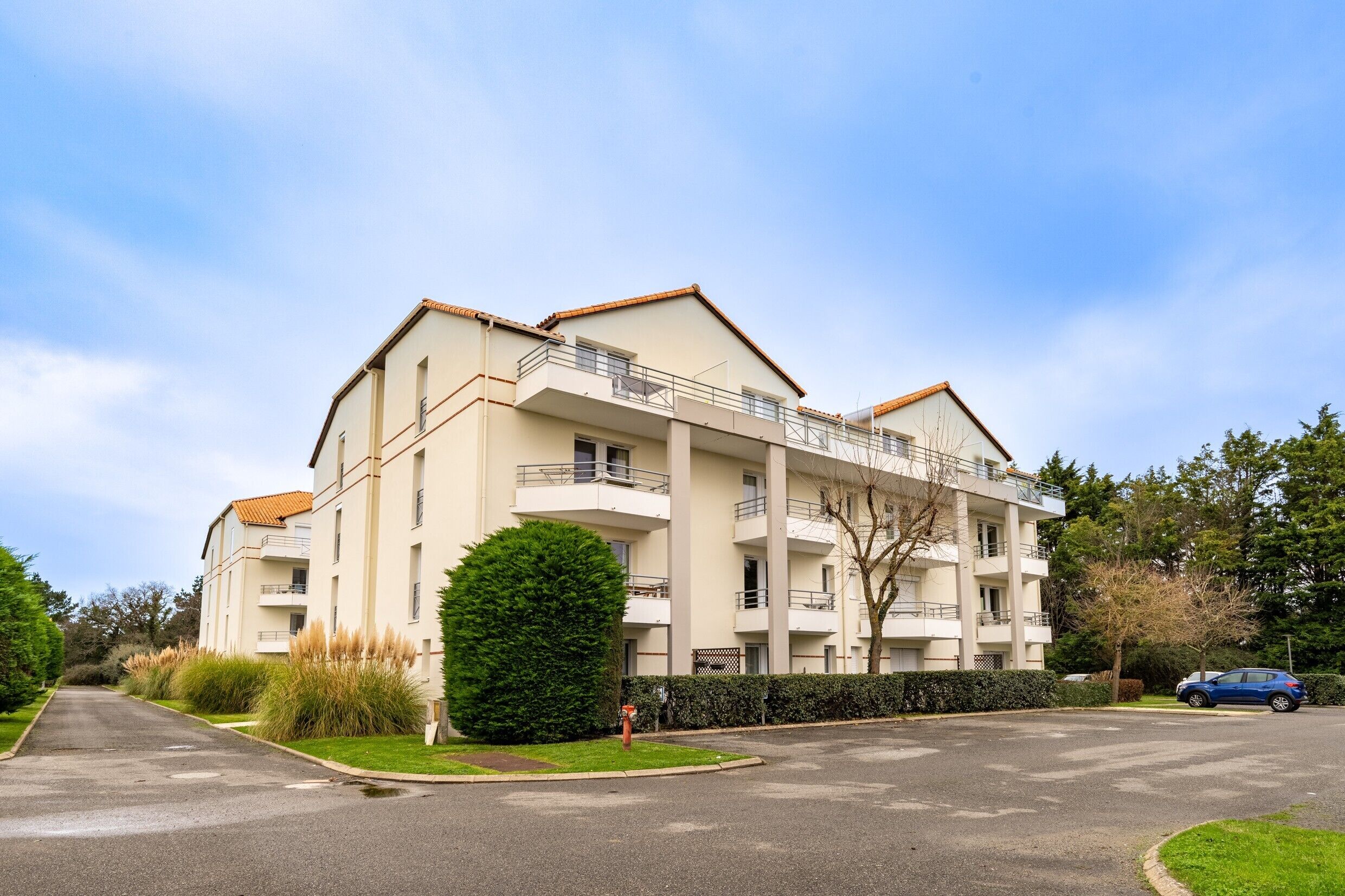 Un immeuble résidentiel à plusieurs étages, doté de balcons, d’un espace de stationnement et d’une pelouse bien entretenue.