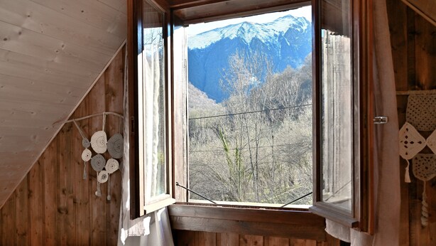 Una habitación con techo de madera, una ventana con cortinas, una cama con almohada estampada y un adorno colgado en la pared.