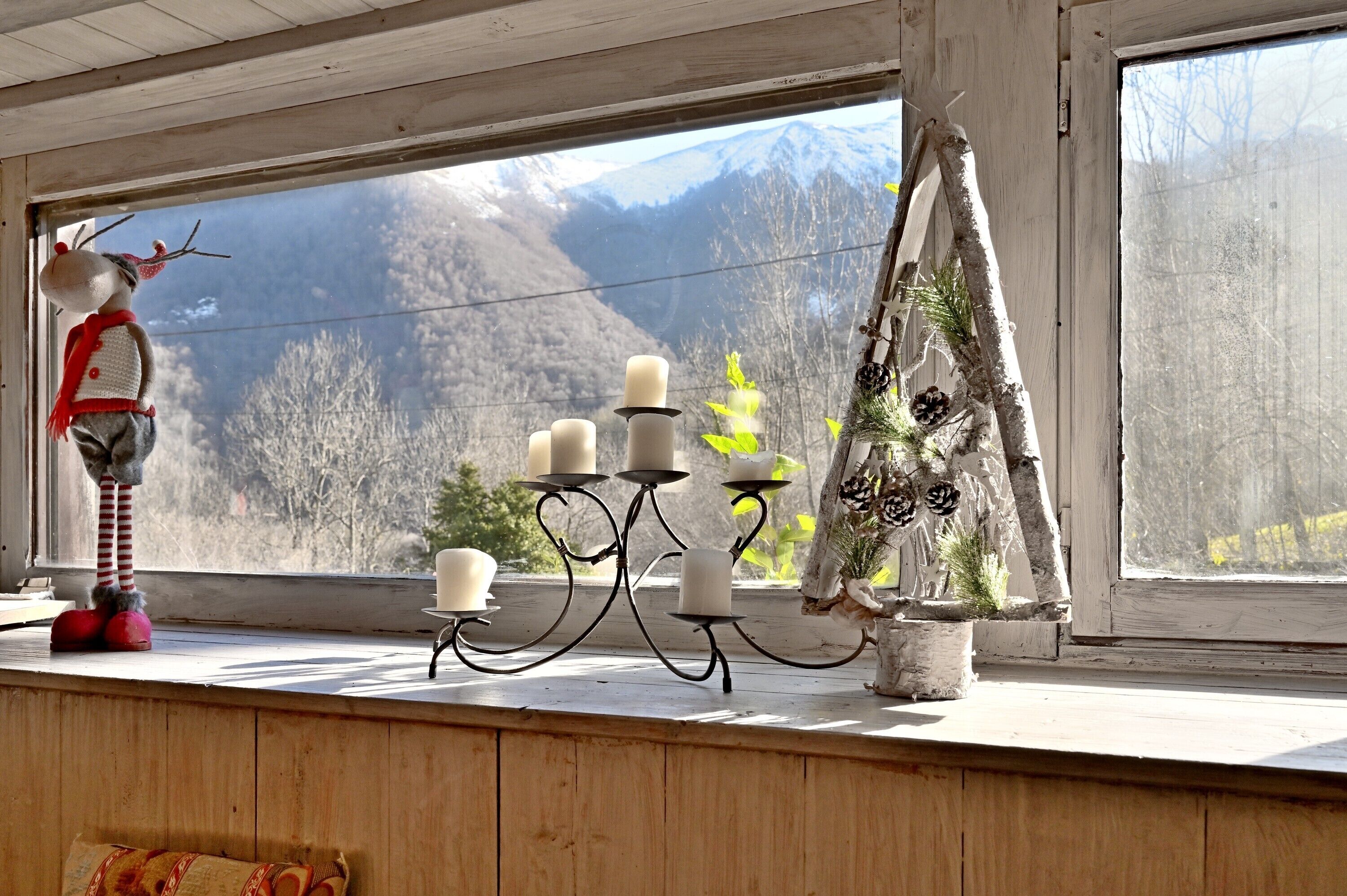Una ventana con vistas a las montañas, un reno decorativo y un candelabro con velas.