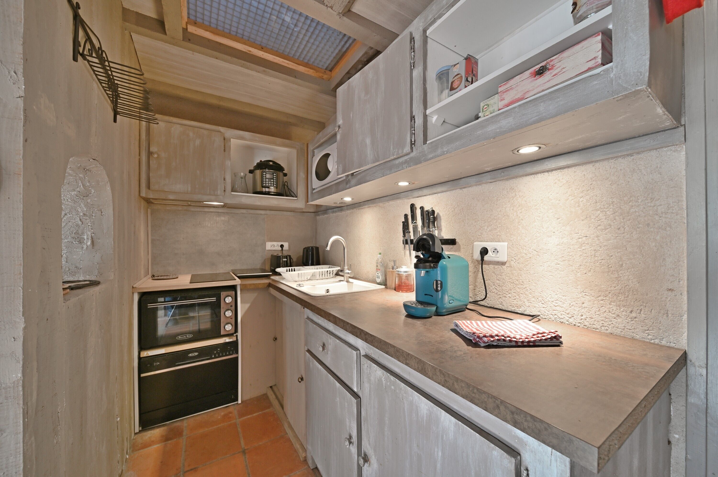 A compact kitchen with a built-in oven, a coffee machine, and a sink.