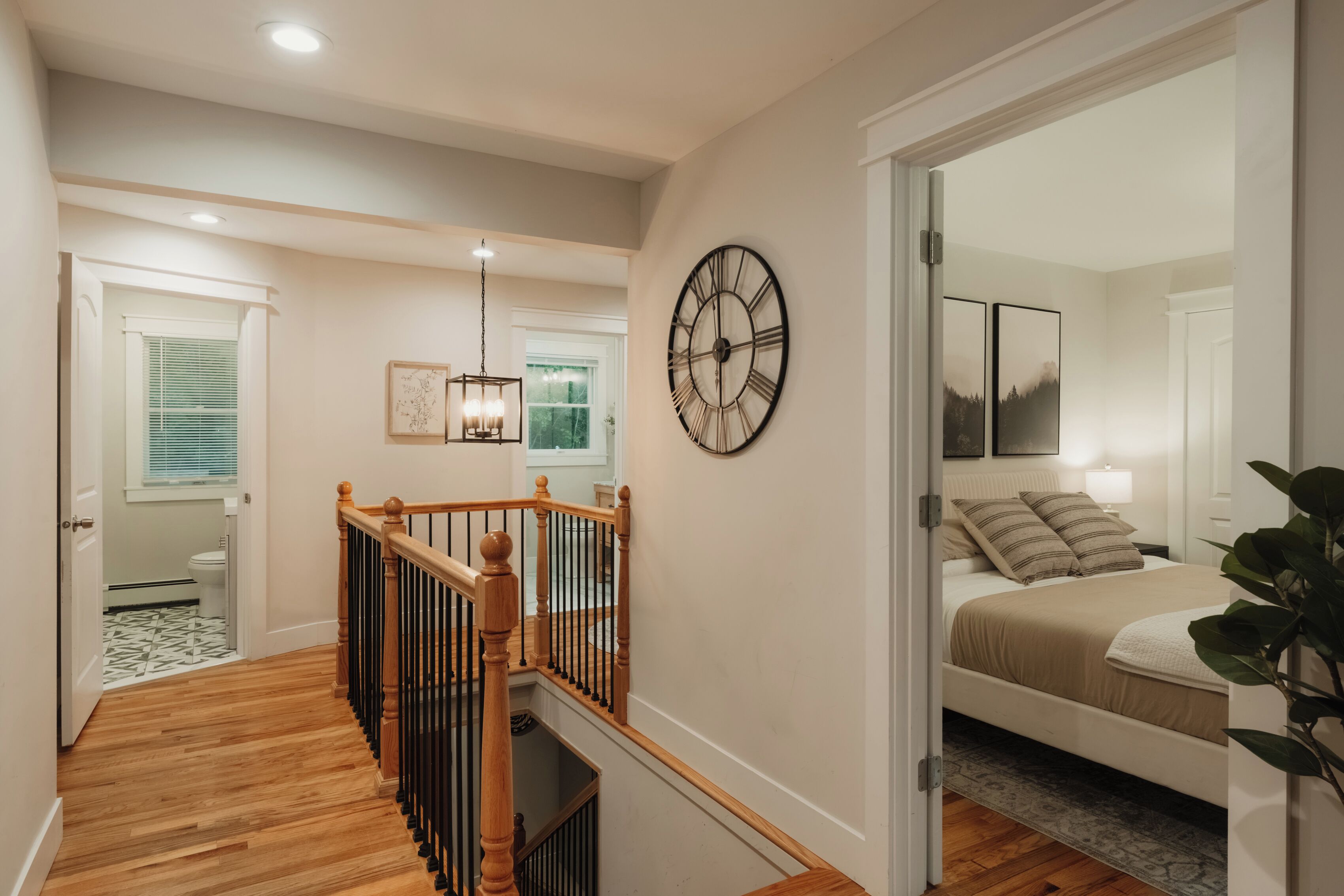 Una escalera conduce a un dormitorio con una cama, un reloj de pared grande y una ventana con persianas.