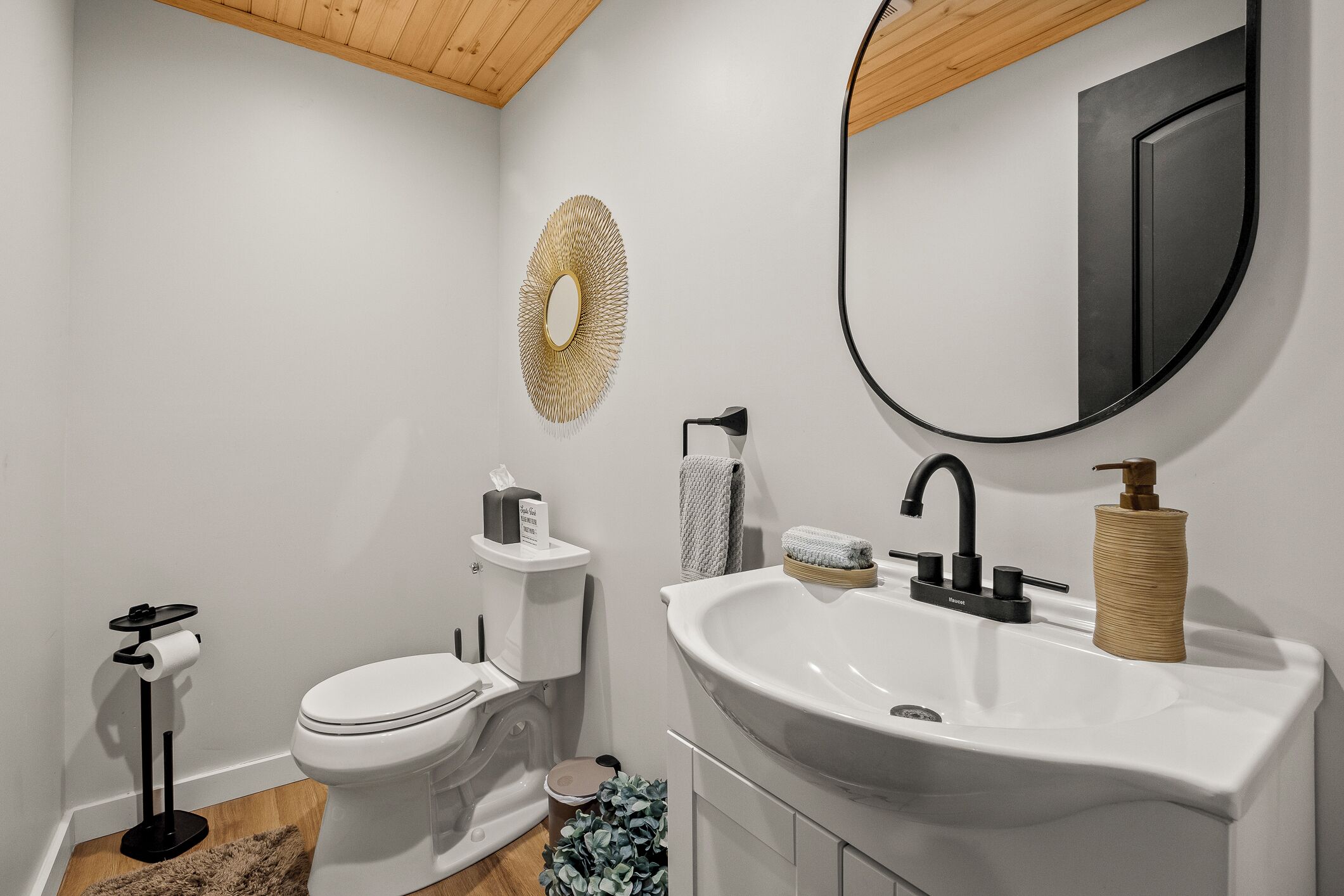 Un bagno moderno con lavandino bianco, rubinetto nero e specchio rotondo.