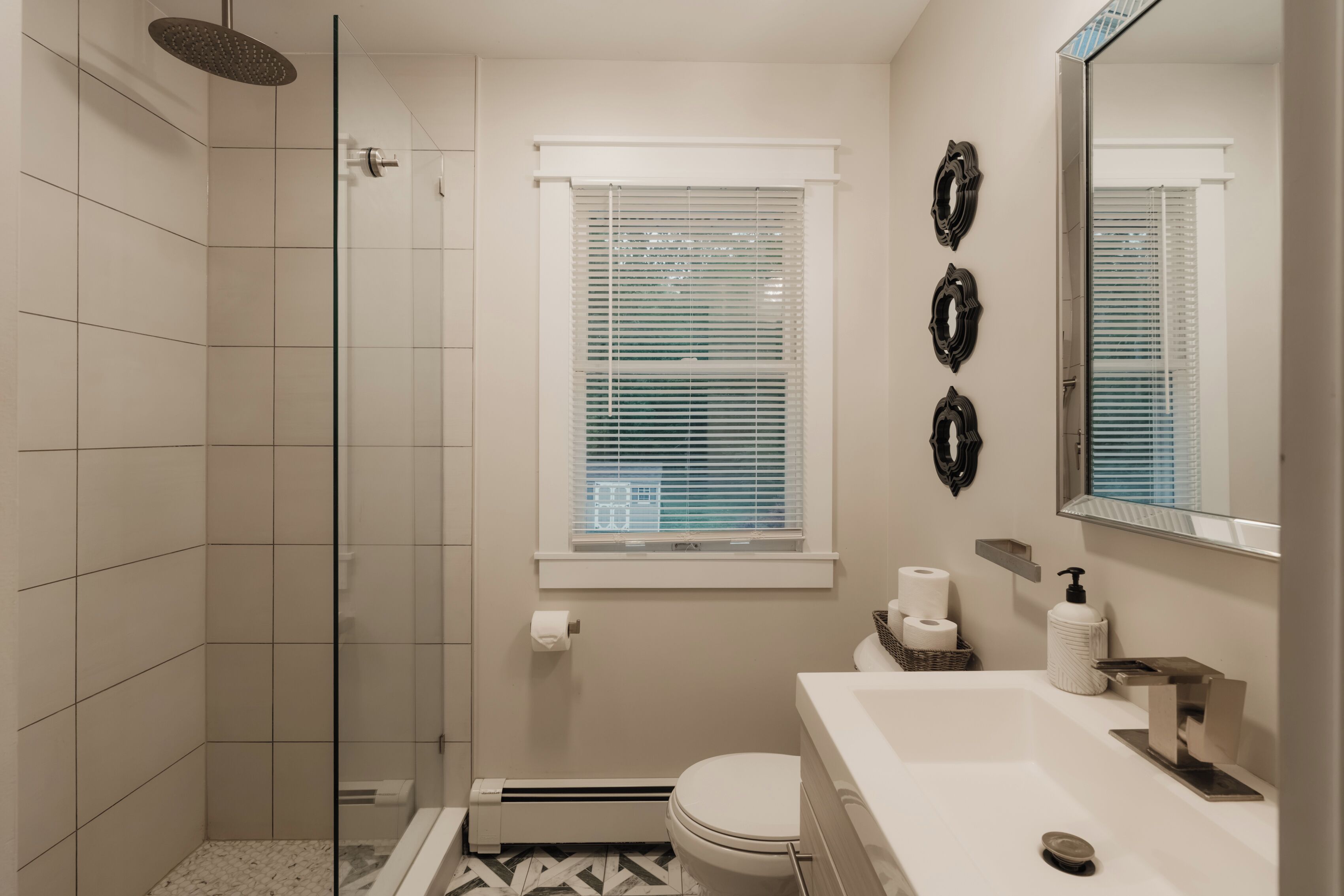 Baño con ducha, inodoro y lavamanos, que incluye una ventana con persianas y decoración en las paredes.