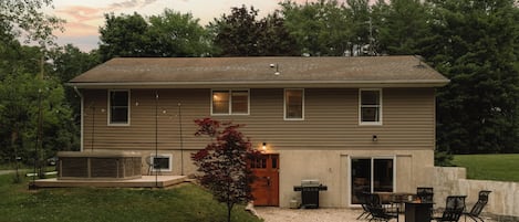 A two-story house with a patio area, outdoor seating, and a small tree.
