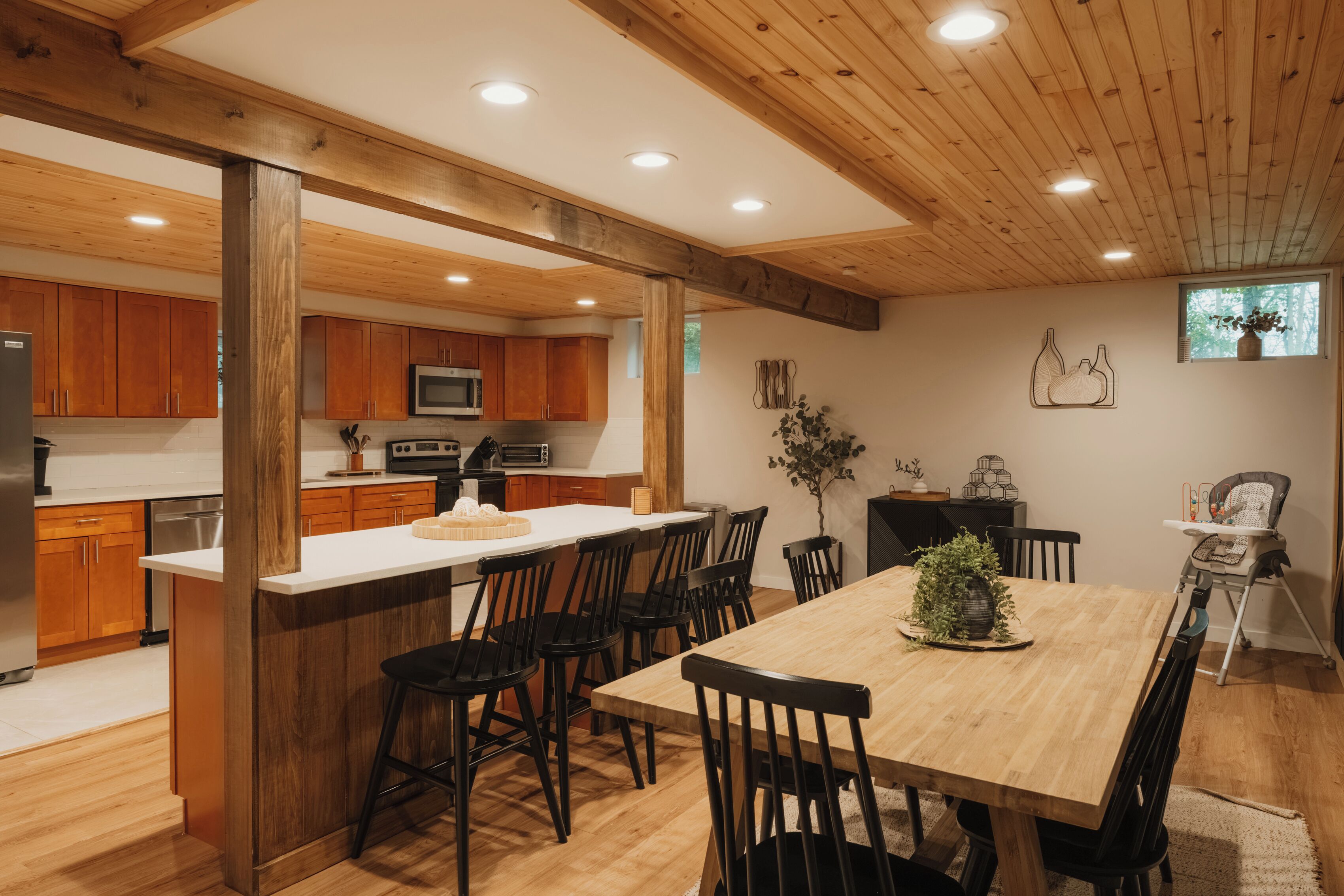 A modern kitchen with wooden cabinets, a central island, and a dining area with a high table and chairs.
