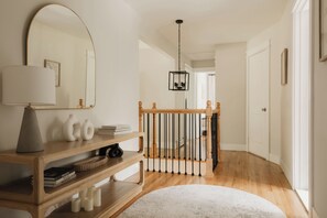 A hallway with a wooden console table, books, a mirror, and a staircase with a black railing.