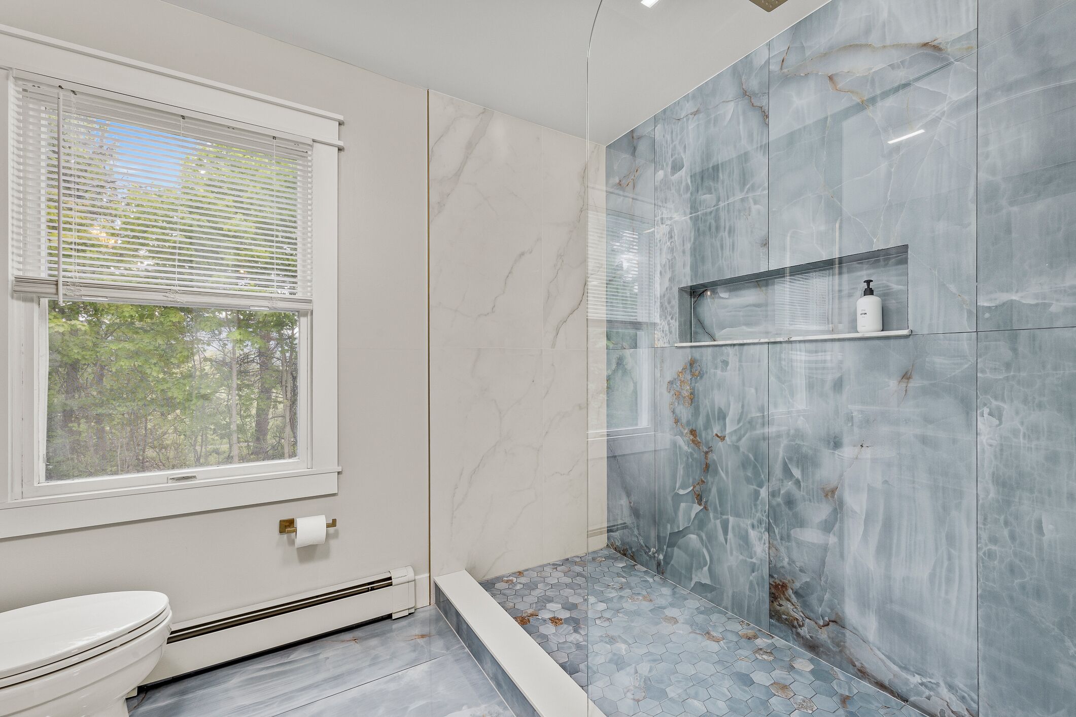 Une salle de bain avec des toilettes, une douche dotée d’une porte en verre et un mur en marbre.