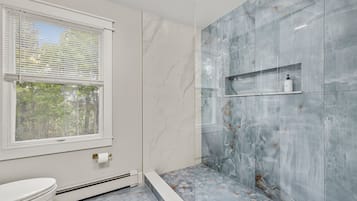 Une salle de bain avec des toilettes, une douche dotée d’une porte en verre et un mur en marbre.