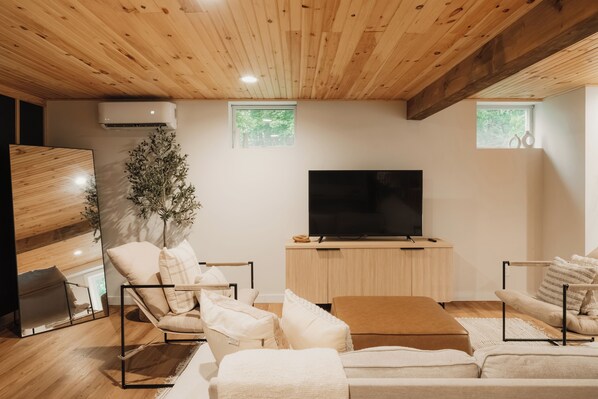 A modern living room with a flat-screen TV, wooden ceiling, and a large window.