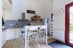 A kitchen with white cabinets, a stove, a sink, and a dining area with two chairs. - Holiday Home 'Home Sweet Home Moliets' with Shared Pool, Private Terrace & Wi-Fi (Moliets-et-Maa)