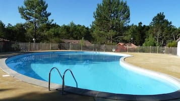Une piscine à bord incurvé, entourée d’une clôture, avec des arbres en arrière-plan.