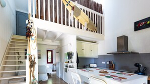 A kitchen with a dining table, chairs, and a staircase leading to a loft. - Holiday Home 'Home Sweet Home Moliets' with Shared Pool, Private Terrace & Wi-Fi (Moliets-et-Maa)