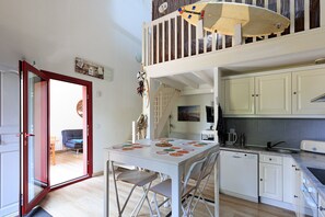 A kitchen with a dining table, white cabinets, and a staircase leading to an upper level. - Holiday Home 'Home Sweet Home Moliets' with Shared Pool, Private Terrace & Wi-Fi (Moliets-et-Maa)