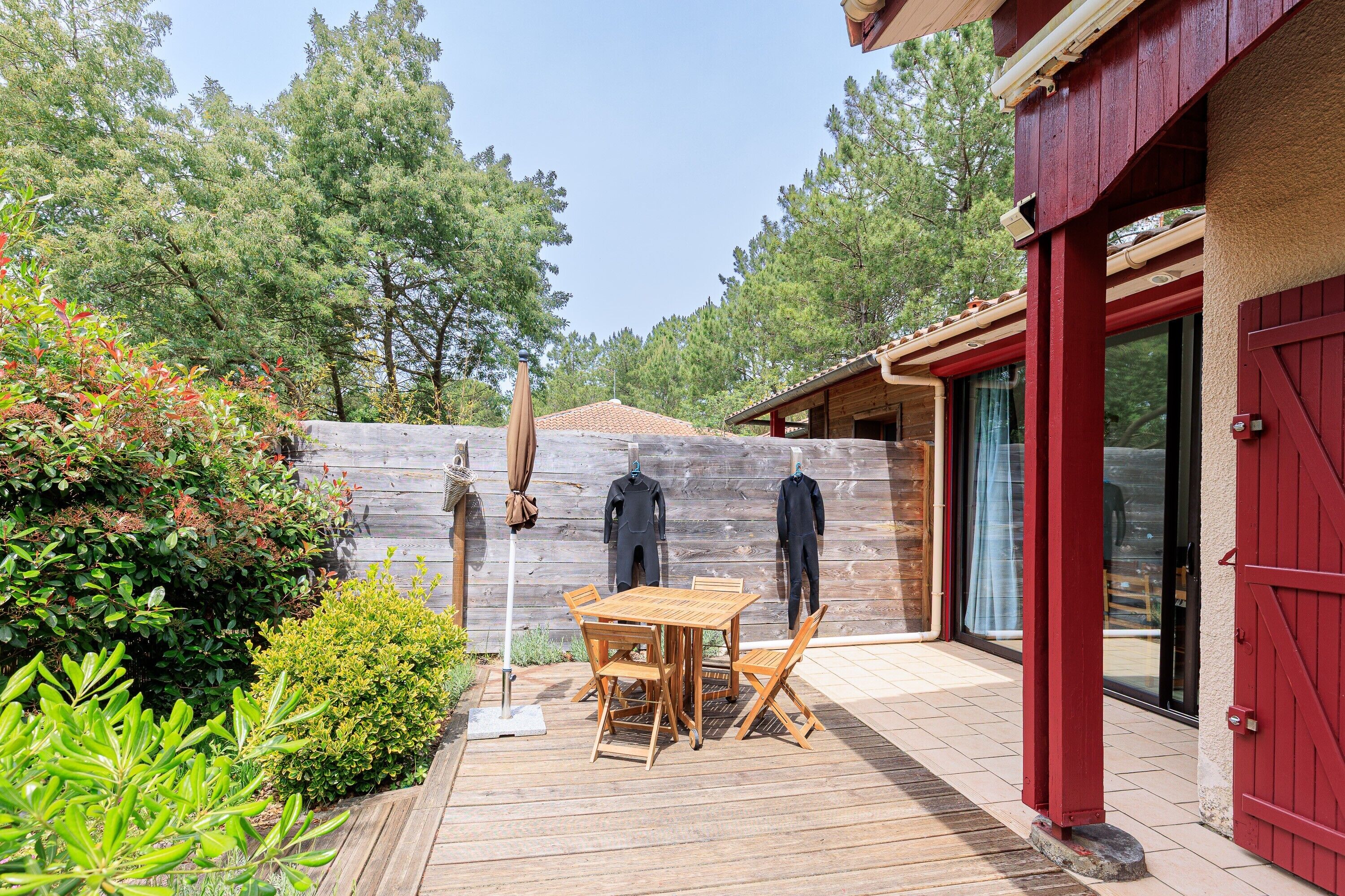 A wooden deck with a table and chairs, surrounded by greenery and a wooden fence.