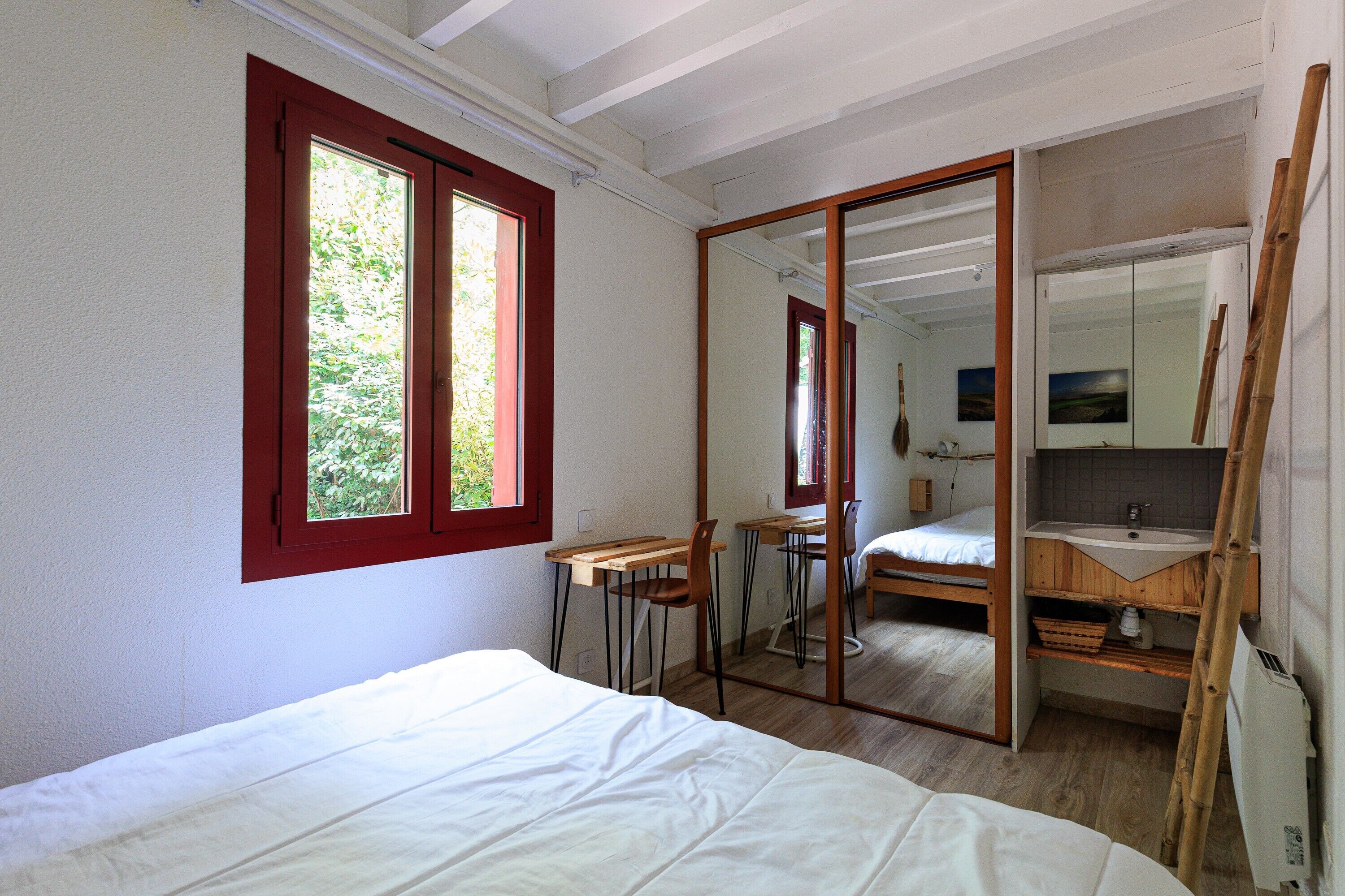 A bedroom with a bed, a desk, a chair, a mirror, and a bathroom with a sink and mirror.
