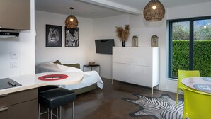 Een moderne kamer met een bed, een bureau, een stoel, een eettafel en een groot raam met uitzicht op groen.