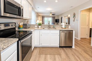 Une cuisine moderne avec des armoires blanches, des appareils en acier inoxydable, un comptoir en granit et un ventilateur de plafond.