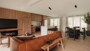 Een moderne woonkamer met een grote flatscreen televisie, een open haard, een bank en een eethoek met een tafel en stoelen.