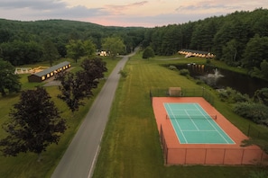 A tennis court adjacent to a building with a view of a lake and forested hills. - Beaver Lodge at Carter Bridge Estate (Freehold)