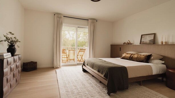 Een slaapkamer met een bed, een dressoir, een raam met gordijnen en uitzicht op de omgeving.