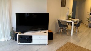 Un soggiorno moderno con una TV a schermo piatto, un piccolo mobiletto bianco e un'area pranzo con tavolo e sedie.