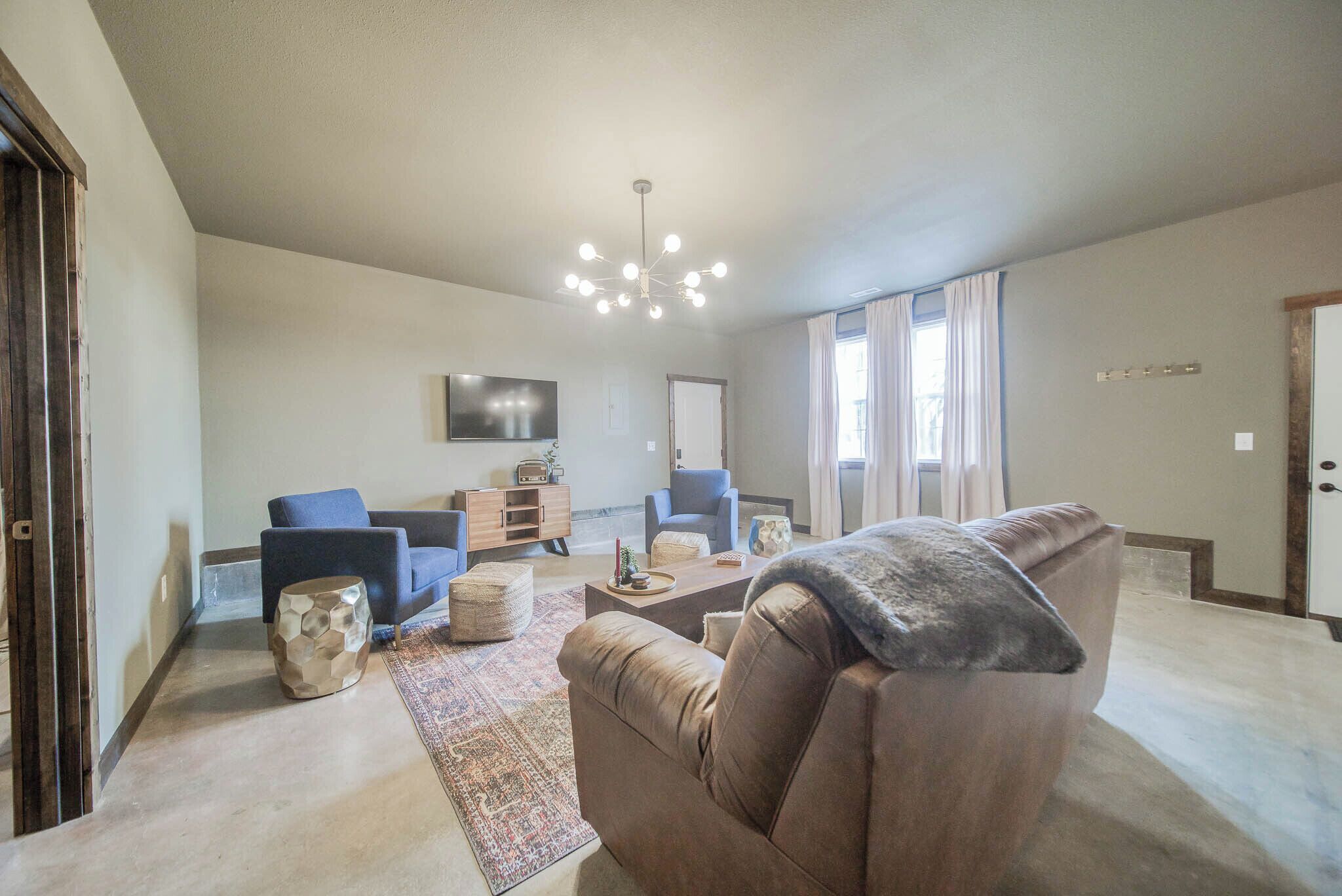 Ein geräumiges Wohnzimmer mit einem braunen Ledersofa, einem blauen Sessel und einem Couchtisch. Eine moderne Kronleuchter hängt von der Decke, und ein Flachbildfernseher ist an der Wand befestigt.
