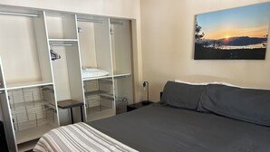 Une chambre à coucher avec un lit, une armoire dotée de plusieurs étagères et un tableau accroch é au mur représentant un coucher de soleil sur des montagnes.