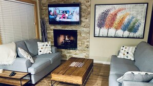 Un salon avec une cheminée, un téléviseur fixé au mur et un tableau abstrait aux couleurs vives.