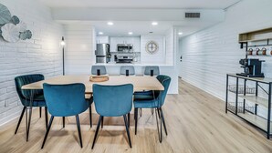 A modern kitchen with white cabinetry, a central island, and a dining area with blue chairs and a wooden table.