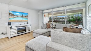 A living room with a sectional sofa, a flat-screen TV, a fireplace, and large windows with a view of the outdoors.