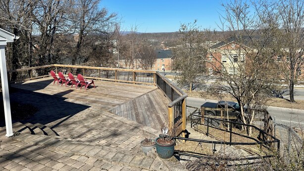 A deck with red chairs, a potted plant, and a view of buildings and trees.