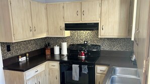 A kitchen with light wood cabinets, a black stove, and a tiled backsplash.