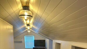 A narrow, wooden-paneled hallway with a staircase leading to a lower level. A flat-screen TV is mounted on the wall in the background.