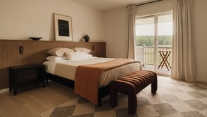Un dormitorio con una cama, mesitas de noche, un banco, un cuadro enmarcado y vistas al exterior.