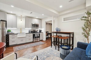 Une cuisine moderne avec des meubles blancs, un four à micro-ondes et un coin repas comprenant un canapé bleu et des chaises en bois.