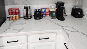 A kitchen with white cabinets, a coffee maker, a blender, and several boxes of coffee and tea.