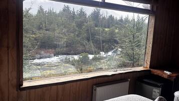 Una habitación con cama, ventana y vista a un bosque, además de aire acondicionado.