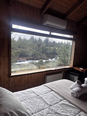 Une chambre avec un lit, une fenêtre donnant sur une forêt et un appareil de climatisation.