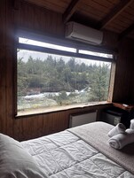 Una habitación con cama, ventana y vista a un bosque, además de aire acondicionado.