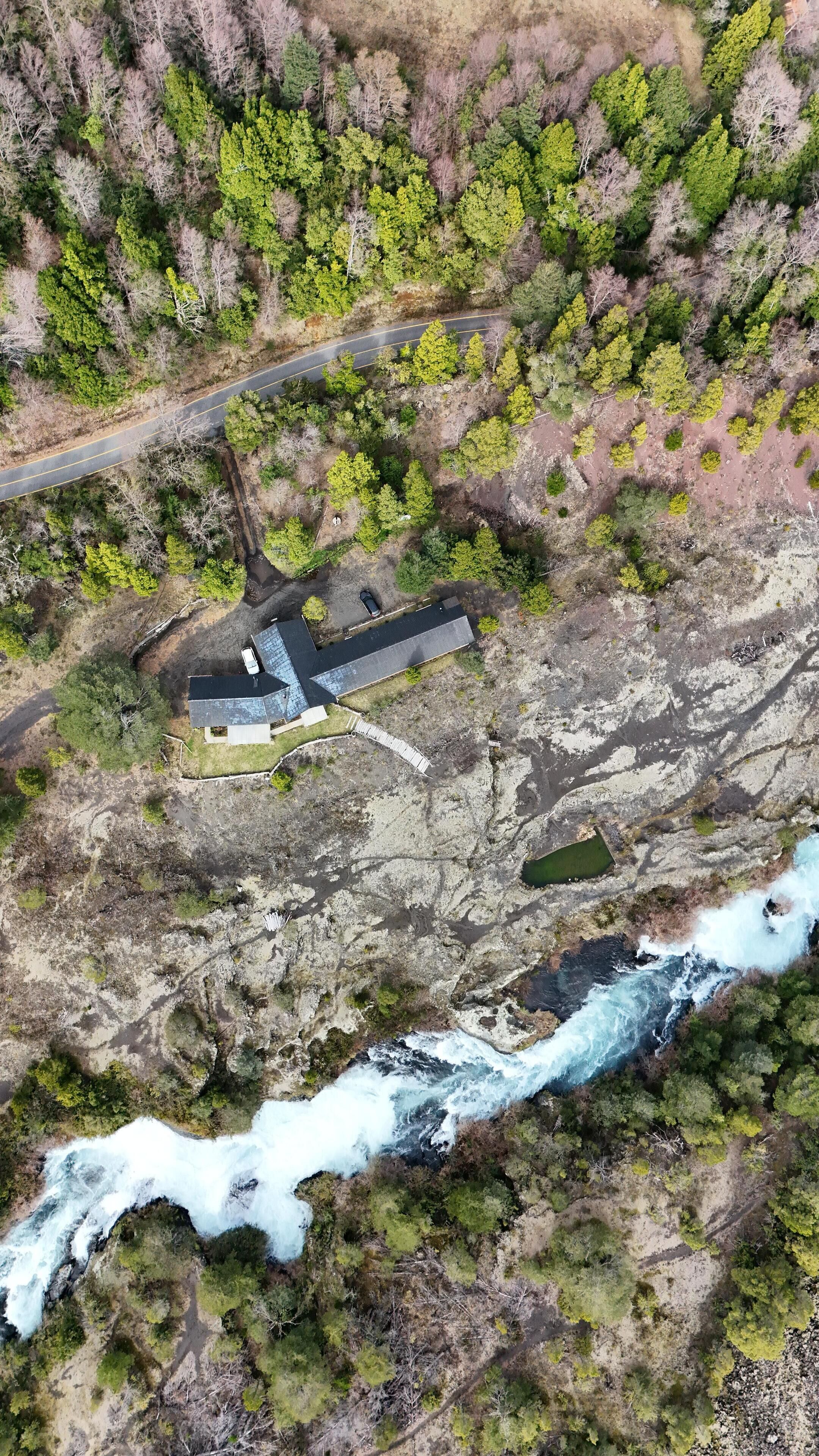 Vista aérea de una cabaña apartada con un pequeño muelle, rodeada de un bosque denso y un río sinuoso.