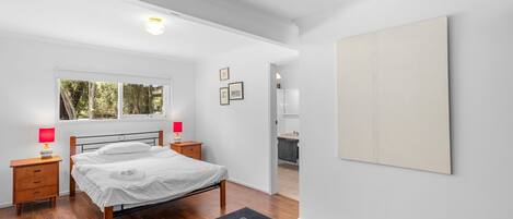 A bedroom with a bed, bedside tables, a window, and a view of the outside.