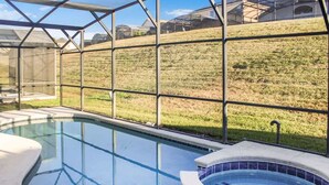 A swimming pool with a glass enclosure, a hot tub, and a grassy hillside in the background.