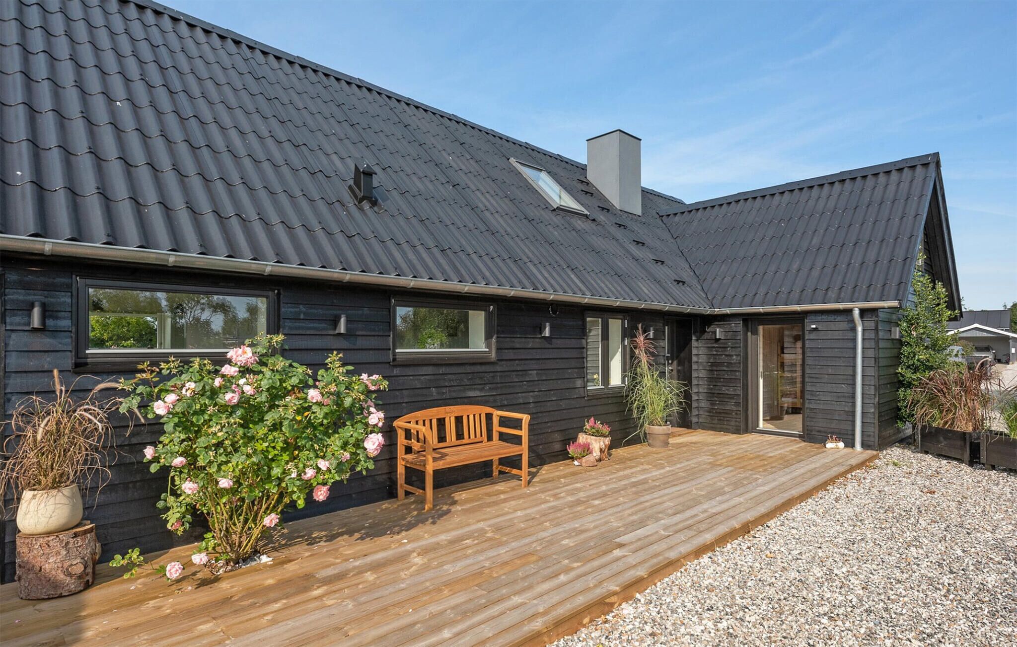 Ein Holzhaus mit dunklem Dach, einer Holzterrasse und einer Bank.