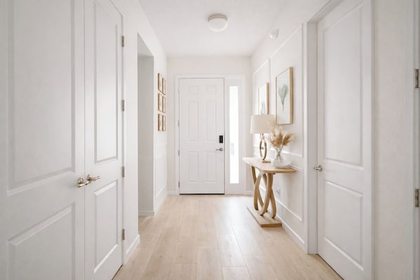A hallway with white doors, a wooden floor, and a console table with a lamp and decorative items.