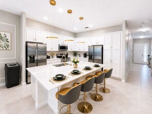 A modern kitchen with white cabinetry, stainless steel appliances, a central island with bar stools, and pendant lighting.
