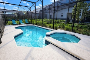 A swimming pool with a hot tub, surrounded by a glass enclosure, and a seating area with chairs.